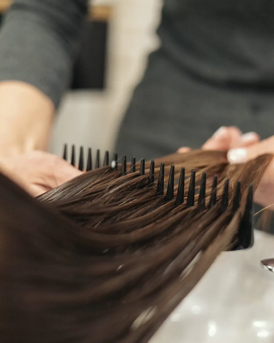 Manos de peluquera sujetando un mechón de pelo liso peinado con peine ancho.